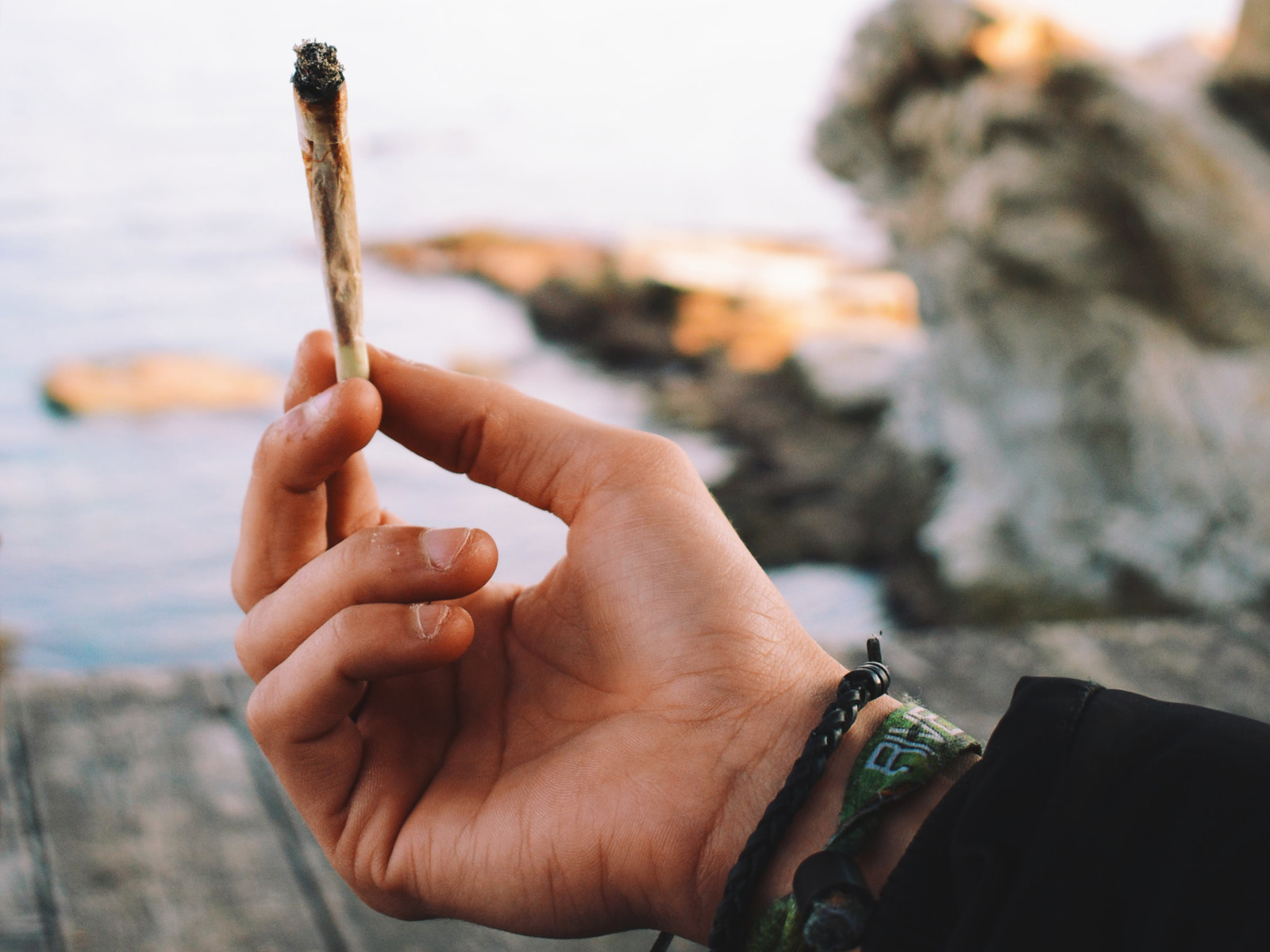 Person holding a cannabis joint at the beach