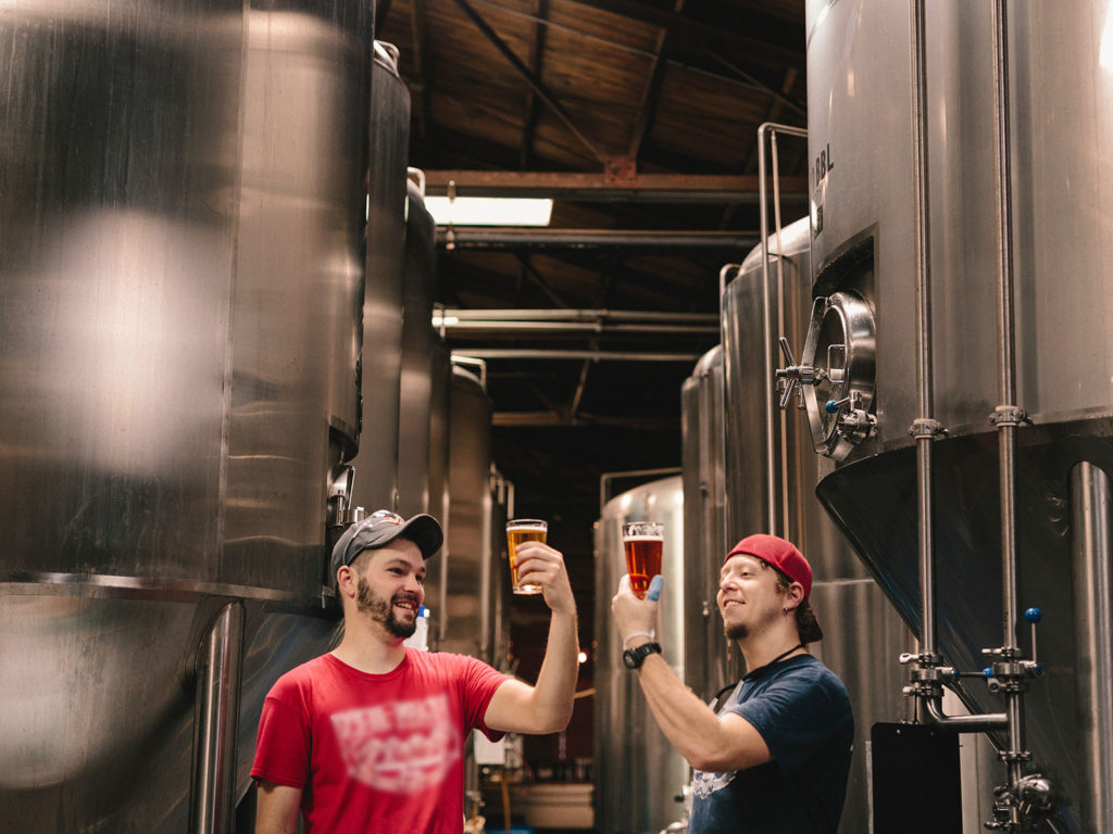 Two men holding glasses of beer in brewery